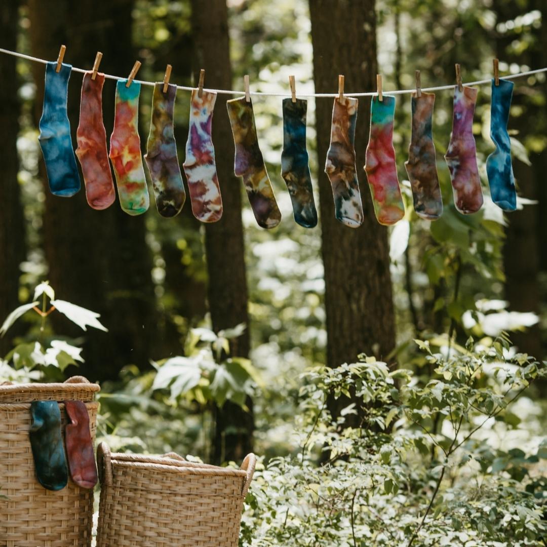 Vibrantly colored ice-dyed cotton socks hanging on an outdoor clothesline with clothespins