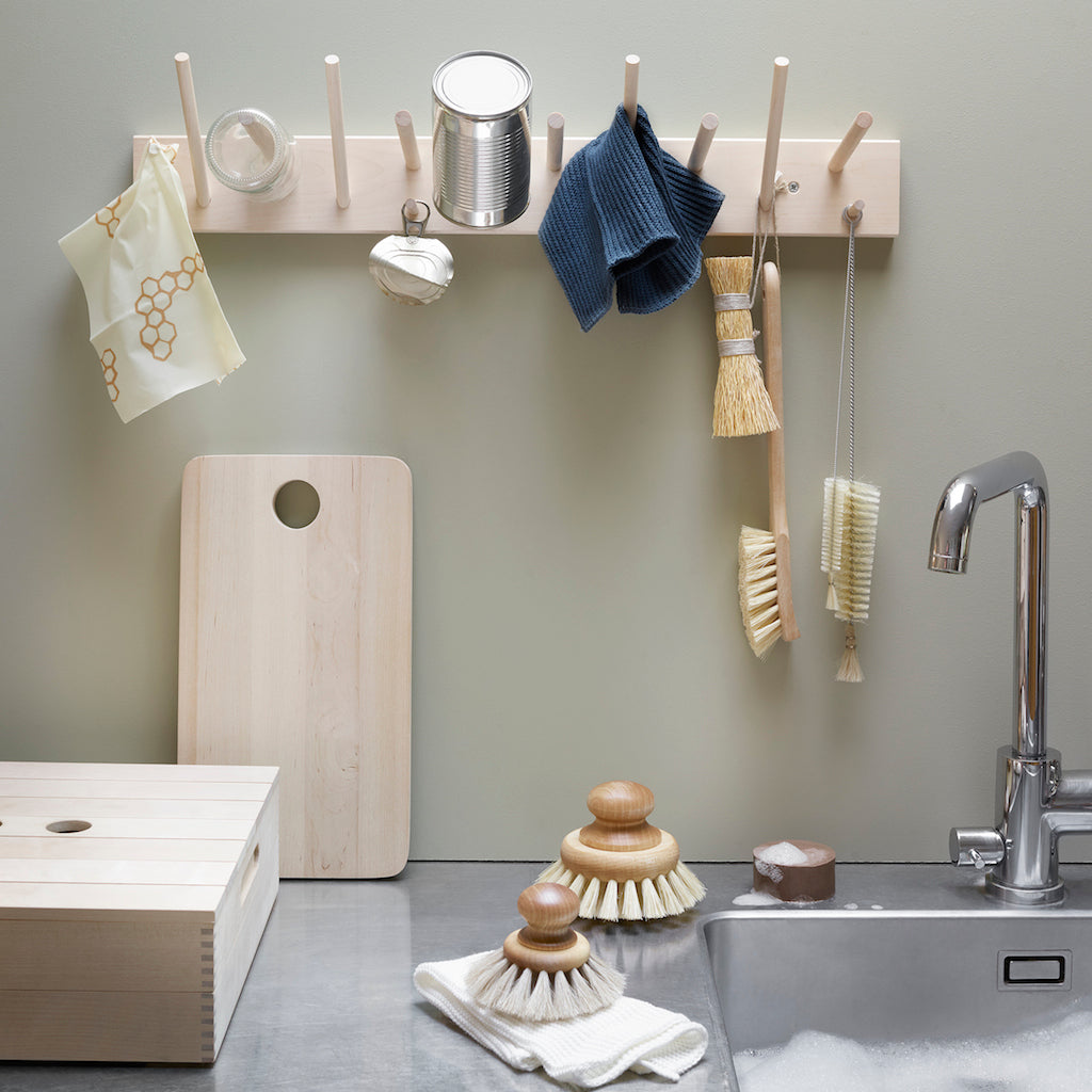 Narrow and long bottle cleaning brushes shown hanging on a wall-mounted peg rail above kitchen sink