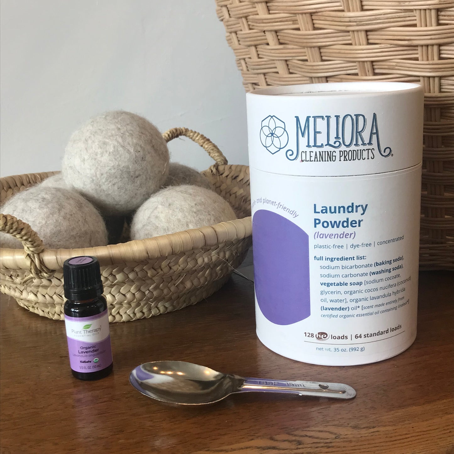 Lavender laundry powder shown with stainless steal scoop (included), wool dryer balls and essential oil