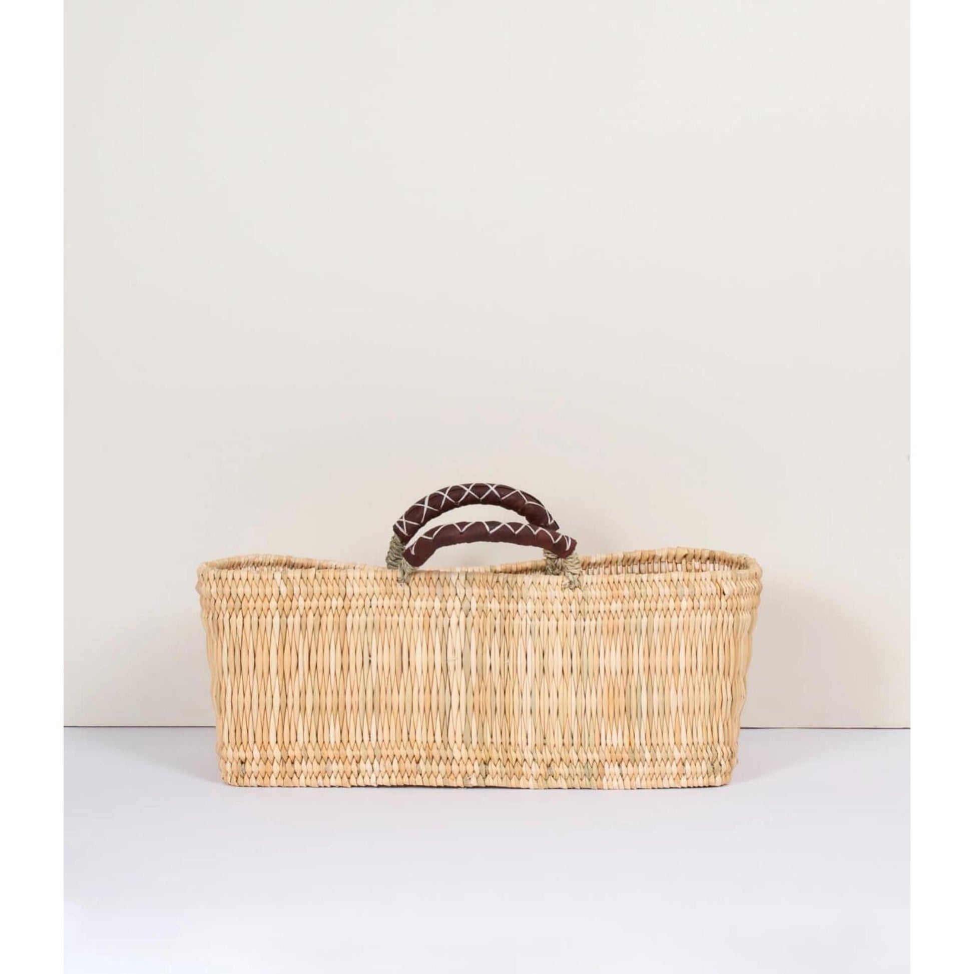 Narrow rectangular handled basket handmade in Morocco with ethically-sourced woven palm leaves and naturally tanned leather shown in large size