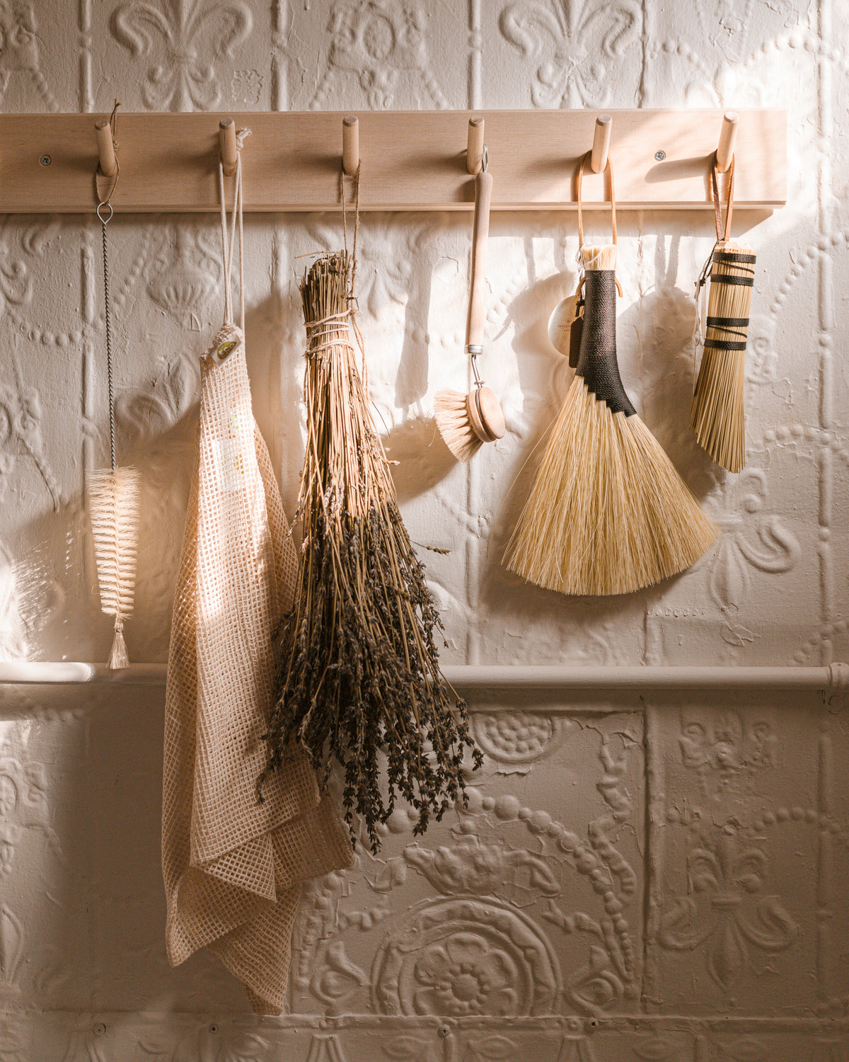Narrow and long bottle cleaning brushes shown hanging on a wall-mounted peg rail 
