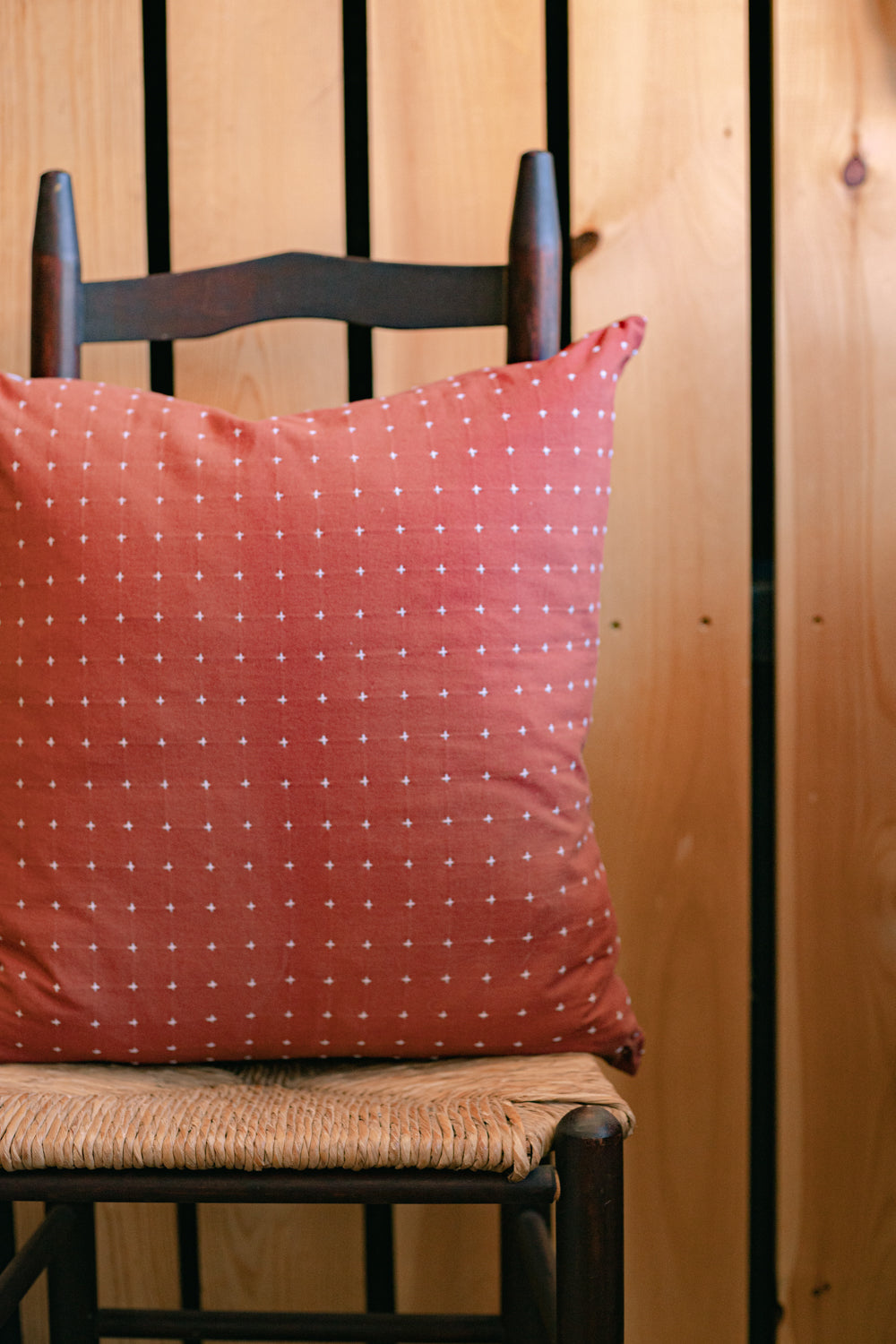 22” hand-embroidered cotton square throw pillow in rust on wooden chair