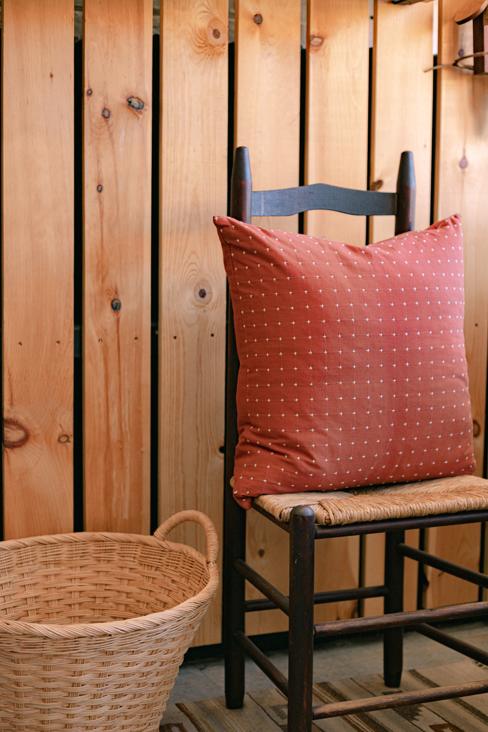 22” hand-embroidered cotton square throw pillow in rust on wooden chair