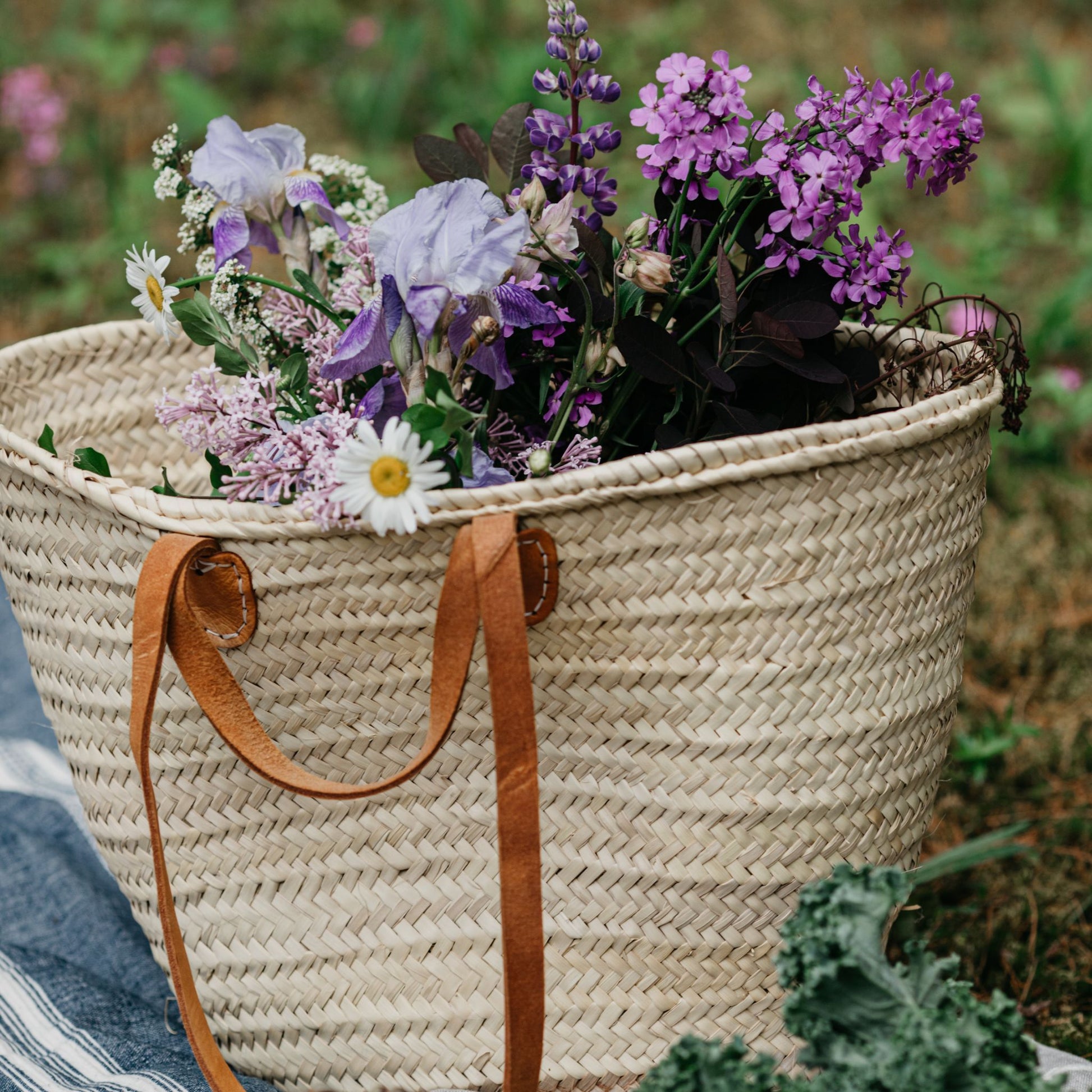 French Market Tote Basket with flowers in it resting on grassland.