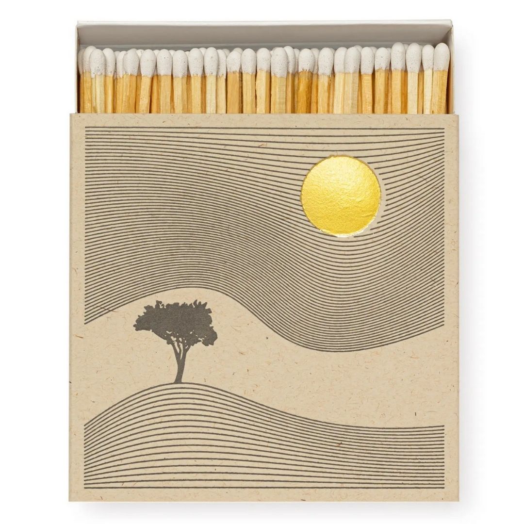 Square box of long wooden matches with image of tree, hill and golden sun